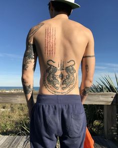 a man with tattoos on his back standing next to a wooden deck near the ocean