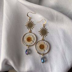 a pair of sunflower earrings on top of a white sheet