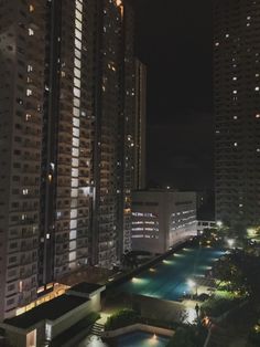 the city is lit up at night with lights on and swimming pool in the foreground