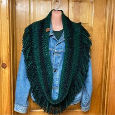 a denim jacket hanging on a wooden door with a green scarf draped over it's shoulders