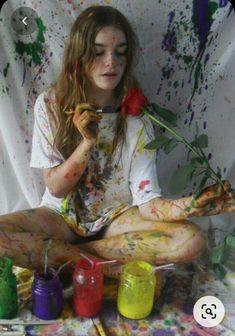 a woman sitting on the ground with paint all over her body and holding a rose