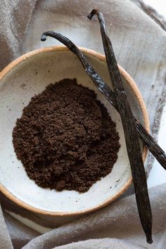 a white bowl filled with dirt next to an unpeeled twig on top of a cloth