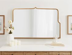 a white dresser topped with a mirror and vase filled with flowers on top of it