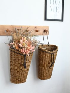 two wicker baskets hanging on the wall with flowers in them and a coat hook