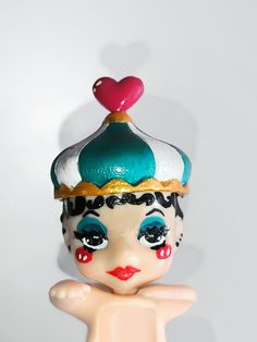 a close up of a toy doll with a heart on its head and hands behind her back