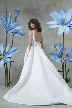 a woman in a white wedding dress standing next to blue flowers with her back turned towards the camera