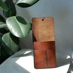 a brown leather case sitting on top of a white table next to a green plant