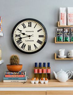 a large clock mounted to the side of a wall next to shelves filled with books and cups