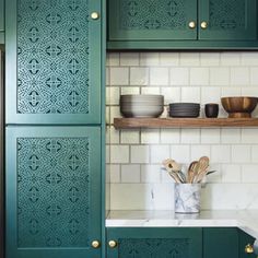 a kitchen with green cupboards and white counter tops in front of a tiled backsplash