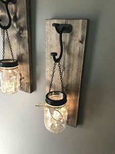 two mason jars are hanging on the wall next to a light fixture that is made out of wood