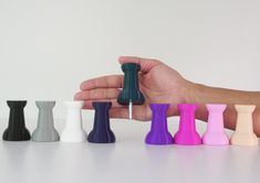 a hand is holding an assortment of small vases in different colors on a white surface