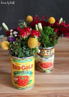 two tin cans filled with flowers on top of a wooden table