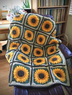 a crocheted blanket with sunflowers is sitting on a leather chair in front of a bookshelf