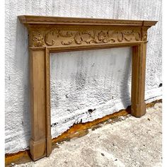 an old fireplace mantle with carvings on the top and bottom, in front of a white stucco wall