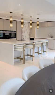 a modern kitchen with marble counter tops and white chairs in the foreground is a dining table that has four bar stools on it