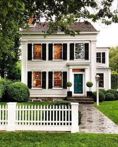 a white house with black shutters on the front and green door, surrounded by trees