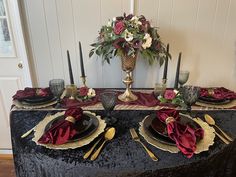 a table set with black and gold place settings, red napkins, and flowers