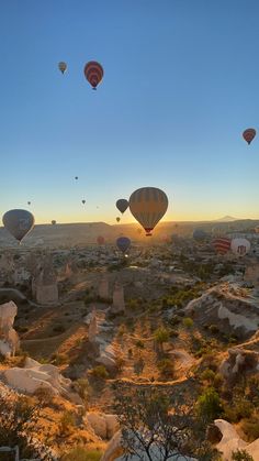 many hot air balloons flying in the sky above some rocks and trees at sunset or dawn