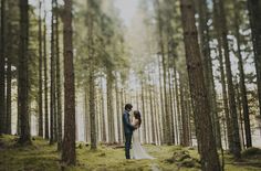 a bride and groom standing in the middle of a forest with their arms around each other