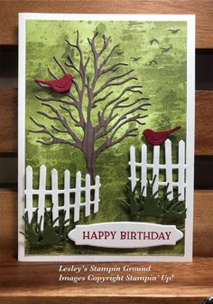 a birthday card with a tree and two birds on it, sitting in front of a fence