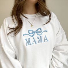 a woman wearing a white sweatshirt with the word mama on it and a blue bow around her neck