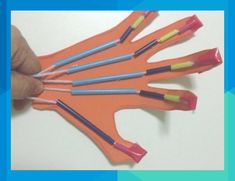 a hand holding an orange piece of paper with colored sticks sticking out of it