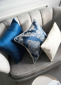 two blue and white pillows sitting on top of a gray couch next to a table