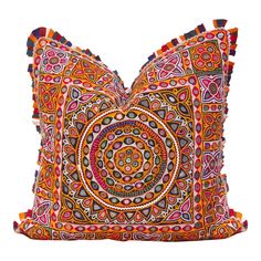 an orange and pink pillow with tassels on the front, sitting on a white surface