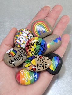 a person's hand is holding some rocks with writing on them and rainbows