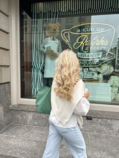 a woman walking down the street in front of a store window with her back to the camera