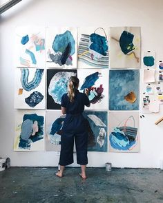 a woman standing in front of a wall with paintings on it