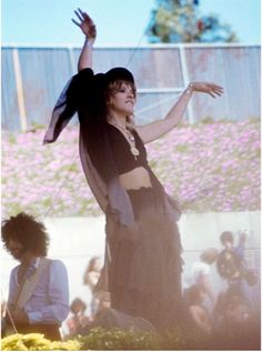 a woman in black dress standing on top of a stage with her arms out to the side