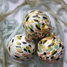 three colorful ornaments are sitting on a white cloth covered tablecloth, one is gold and the other is green