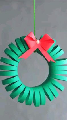 a paper wreath with a red bow hanging from it's center and green ribbon