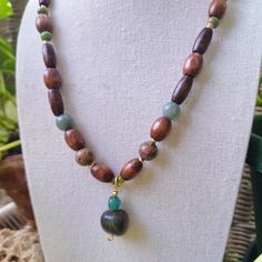 A Long Earthy Bohemian Gemstone And Wood Beaded Necklace. Crafted With Green Ceramic Beading, Natural Varnished Wood Tube And Barrel Beading, Polished Green Jade Stone, Polished Green Unakite Stone, 4 Mm Green Glass Beading, And A Unique Pendant Made Of Ocean Blue Tourmaline Stone And A Striking Tumbled Dark Green River Jasper Stone. Handmade By Me, One Of A Kind. Hypoallergenic Stainless Steel Chain And Clasp. Nickel Free. Total Length: 21 Inches Length Of Chain: 19.5 Inches Extender Length: Ha Earthy Necklace, Earthy Bohemian, Ocean Necklace, Wood Bead Necklace, Green River, Hippie Necklace, Amethyst Gold, Blue Tourmaline, Rose Pendant