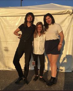 three young women standing next to each other in front of a white sheet covered tent