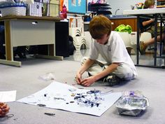 two young boys are sitting on the floor working on their art project in an office