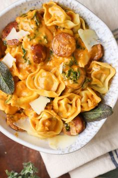 a white bowl filled with pasta and meat on top of a wooden table next to a napkin