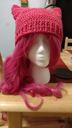 a wig with pink hair and a knitted hat on top of a wooden table