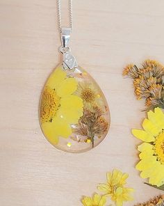 This exquisite handcrafted necklace features real dried flowers, delicately preserved in clear resin. The necklace is truly one-of-a-kind, showcasing a unique blend of yellow flowers and silver leaf, elegantly suspended on a solid 925 sterling silver chain. Details: Chain Material: 925 Sterling Silver Clasp Material: 925 Sterling Silver Flower Setting: Clear Resin Chain length: 18inches  Please note that due to the natural variation of each flower, your necklace may differ slightly from the imag Yellow Sterling Silver Flower Jewelry, Sterling Silver Necklaces With Pressed Flowers, Yellow Birth Flower Pendant Necklace, Yellow Necklace With Birth Flower Pendant, Yellow Pressed Flowers Jewelry, Silver Sterling Silver Necklace With Pressed Flowers, Sterling Silver Teardrop Necklace With Natural Inclusions, Yellow Sterling Silver Necklace With Round Pendant, Yellow Sterling Silver Round Pendant Necklace