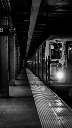 black and white photograph of a subway train at the station with its lights on,