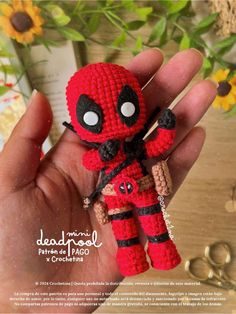 a hand holding a small crocheted deadpool doll