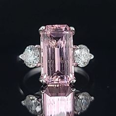 a pink and white diamond ring sitting on top of a black surface with three diamonds around it