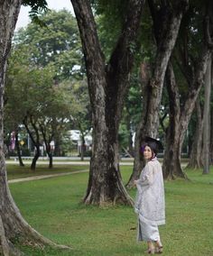 a woman standing in the grass next to some trees