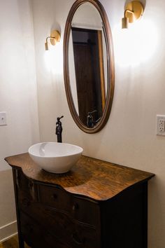 a bathroom sink sitting on top of a wooden dresser next to a large round mirror