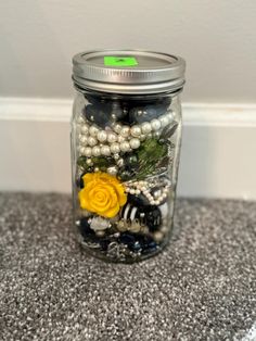 a jar filled with beads and flowers on top of a carpeted floor next to a wall