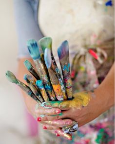 a woman holding lots of paintbrushes in her hands with different colors on them