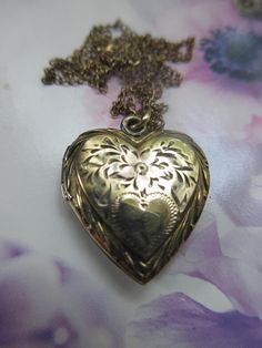 Vintage heart locket necklace in gold fill on silver with a Carl Art makers mark. This pretty heart locket is crafted with a puffed style with engraved flowers accenting a single heart cartouche. Tiny leaves and a detailed border offer the quality of the craftsmanship of a vintage piece. The heart is not monogrammed with initials and can be personalized if you so choose. Inside you will find two spots for photos with frames but no covers. This heart shaped keepsake locket measures seven eighths of an inch by .75'' with the bail. It suspends from an app. 16- 5/8'' fine link chain that is stamped for gold fill on the clasp. The locket exhibits slight wear that adds to the charm of this older vintage piece. Just lovely for a first locket and a lovely accessory to accent romantic and feminine Heart Necklace With Picture Inside, Antique Jewelry For Valentine's Day Anniversary Gift, Antique Jewelry For Anniversary Gift On Valentine's Day, Vintage Double Heart Engraved Necklace, Victorian Engraved Necklaces For Anniversary Gift, Victorian Engraved Necklace For Anniversary, Victorian Engraved Necklace For Anniversary Gift, Antique Heart Jewelry For Anniversary, Antique Heart-shaped Necklace For Anniversary