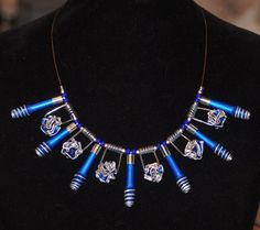 the necklace is decorated with blue beads and silver metal tubes on a black mannequin