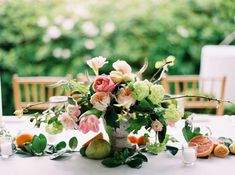 a vase filled with flowers and fruit sitting on top of a white table covered in greenery